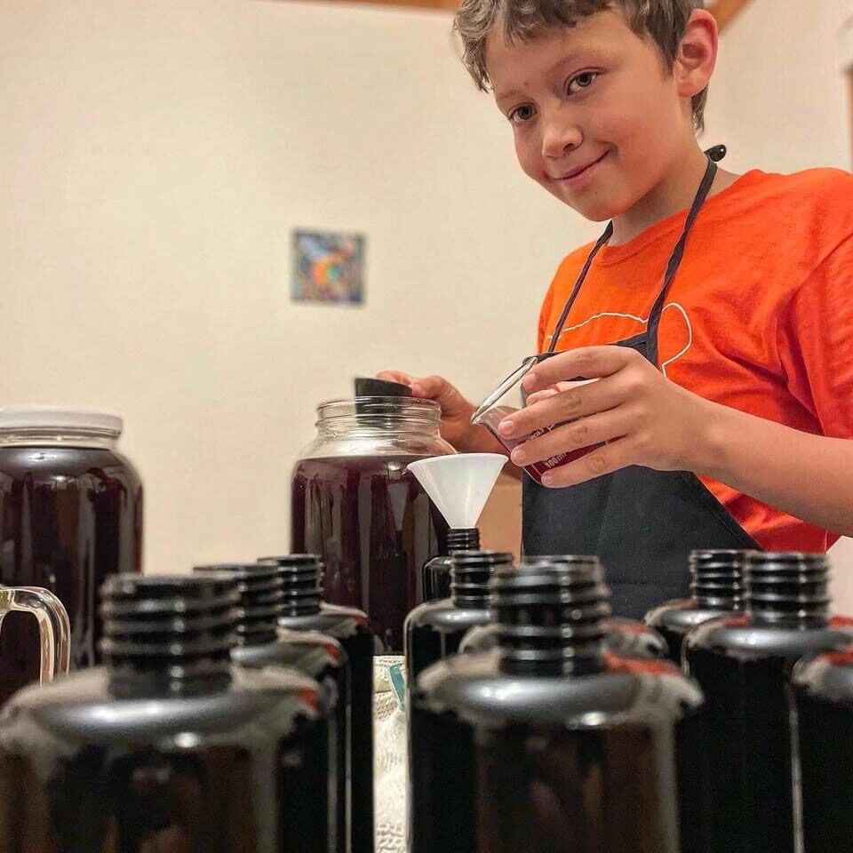 Kai bottling fire cider, surrounded by dark glass bottles